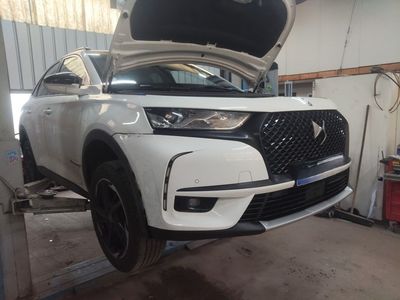 Un SUV DS blanc, capot ouvert, est surélevé sur un pont élévateur dans un atelier automobile lumineux.