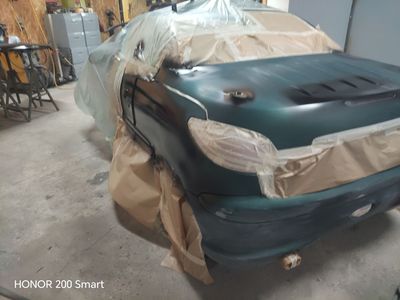 Une voiture verte, masquée avec du ruban adhésif et du papier kraft, est en cours de peinture dans un garage.