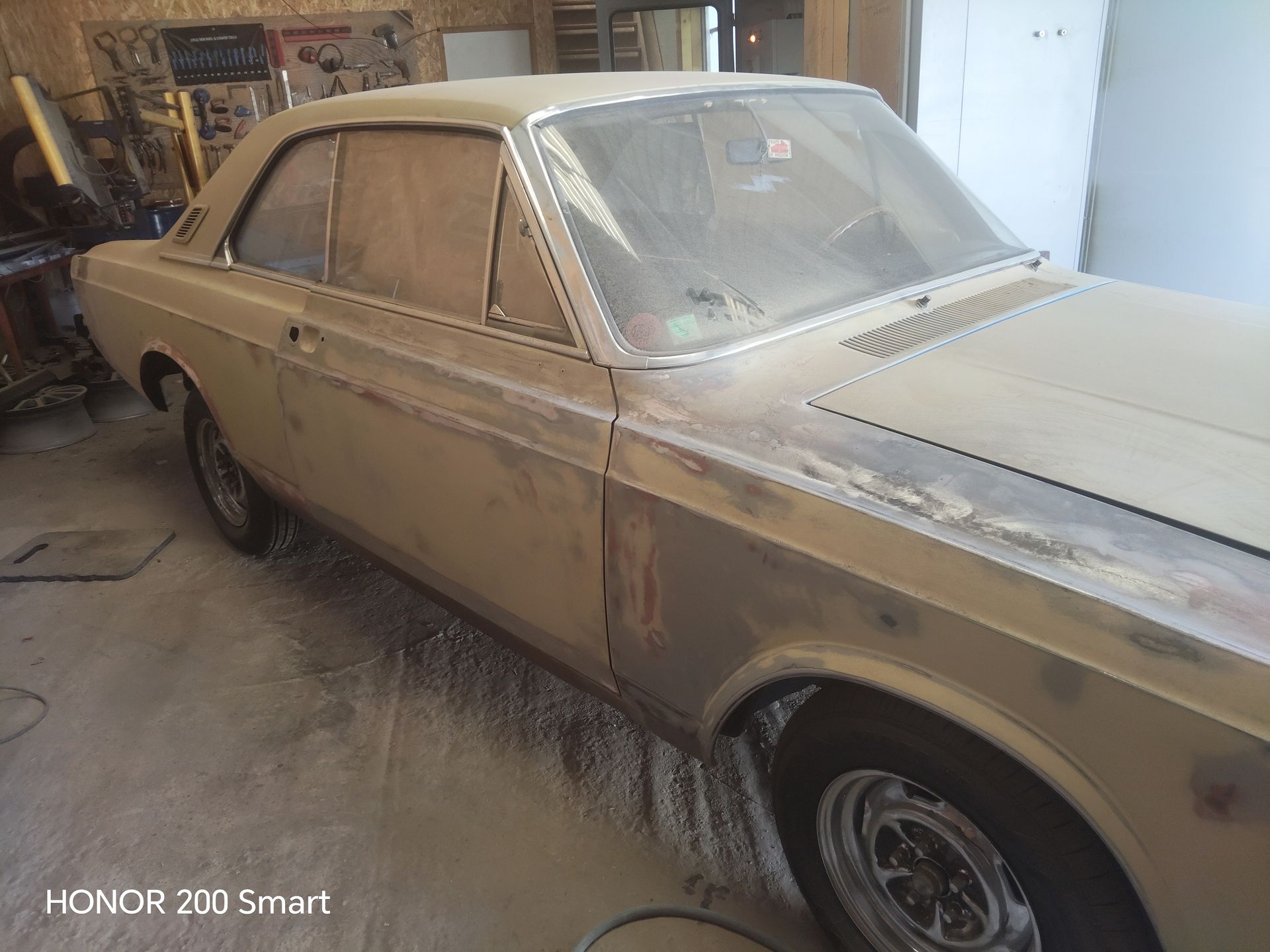Une voiture ancienne deux portes dans un atelier, recouverte de poussière et en cours de préparation de la carrosserie avant peinture.