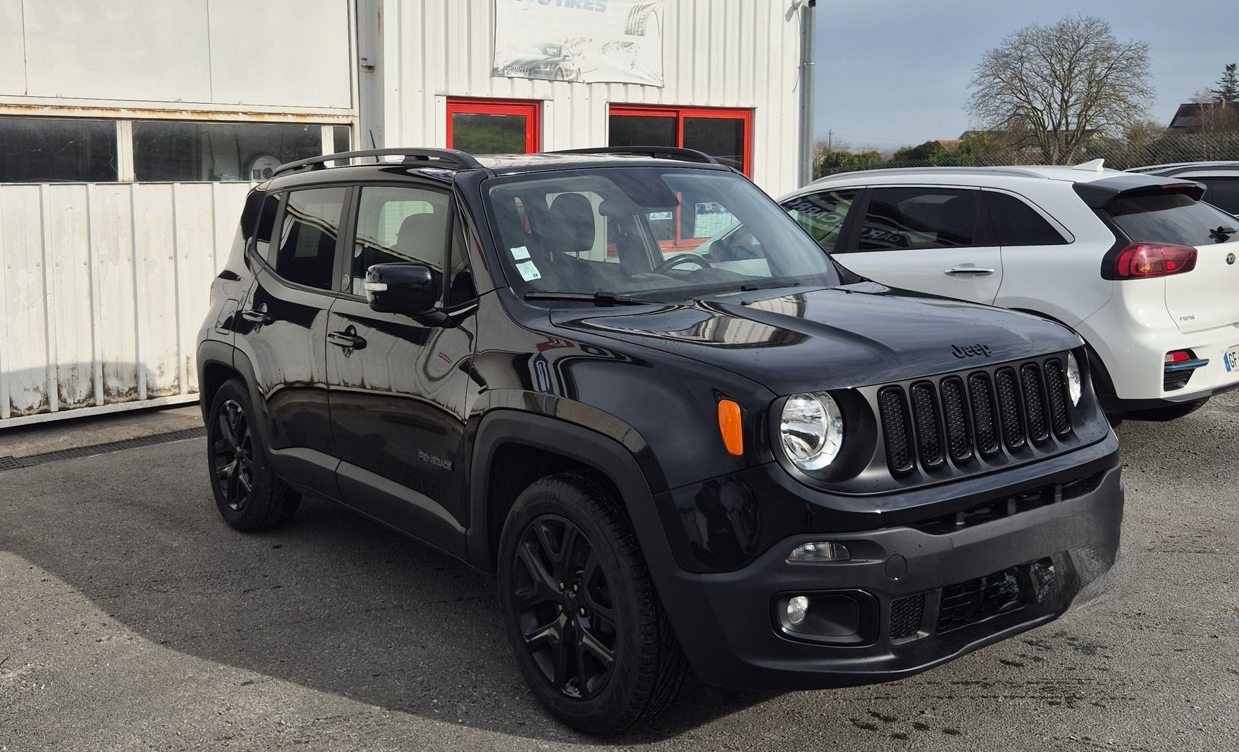 Jeep noire garée devant un bâtiment, avec des voitures blanches en arrière-plan.