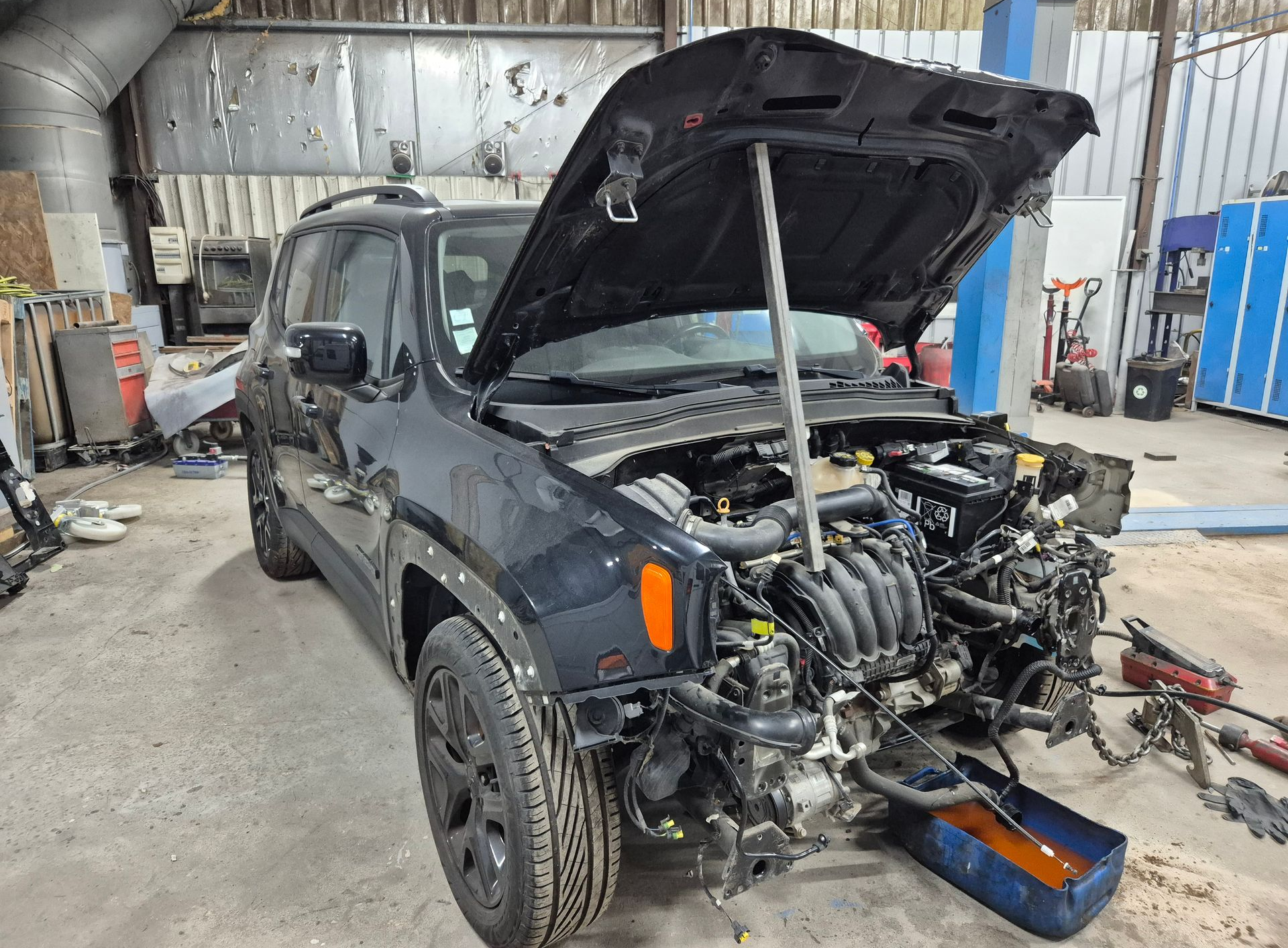 SUV tout-terrain gris dans un garage, capot ouvert et partie avant démontée pour réparation