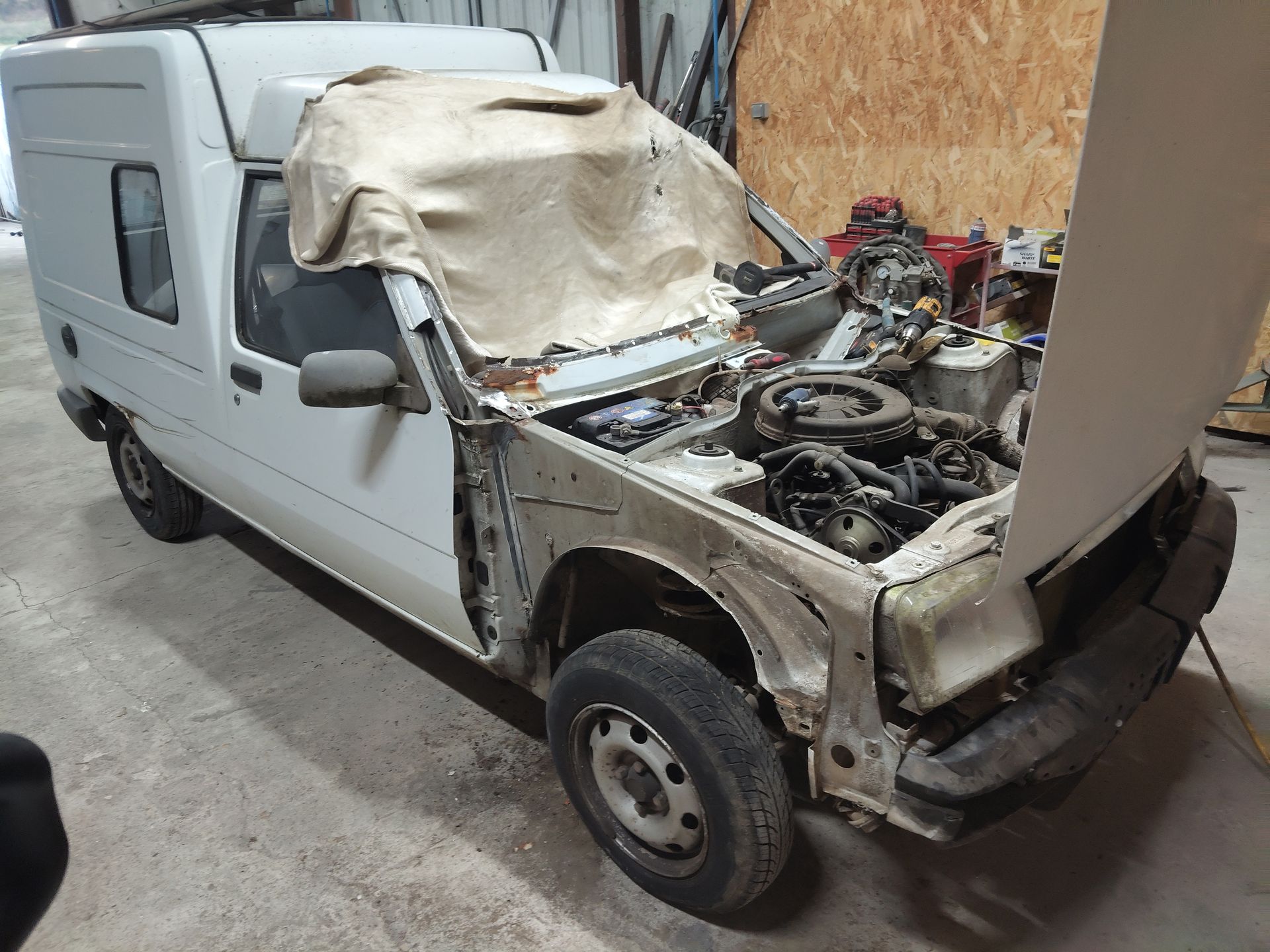 Une camionnette blanche dont l'avant a été démonté, laissant apparaître des pièces du moteur dans un garage d'atelier.