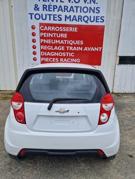 Vue arrière d'une Chevrolet  blanche garée devant une enseigne de garage automobile en français.