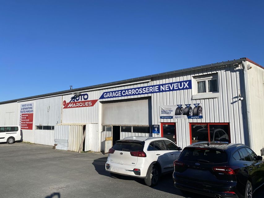 Façade blanche d'un garage automobile avec des enseignes françaises et des voitures garées sous un ciel bleu