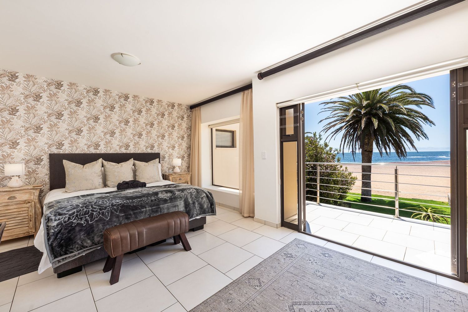 Bedroom with bed, floral wallpaper, and open doors to a beach view with palm tree.