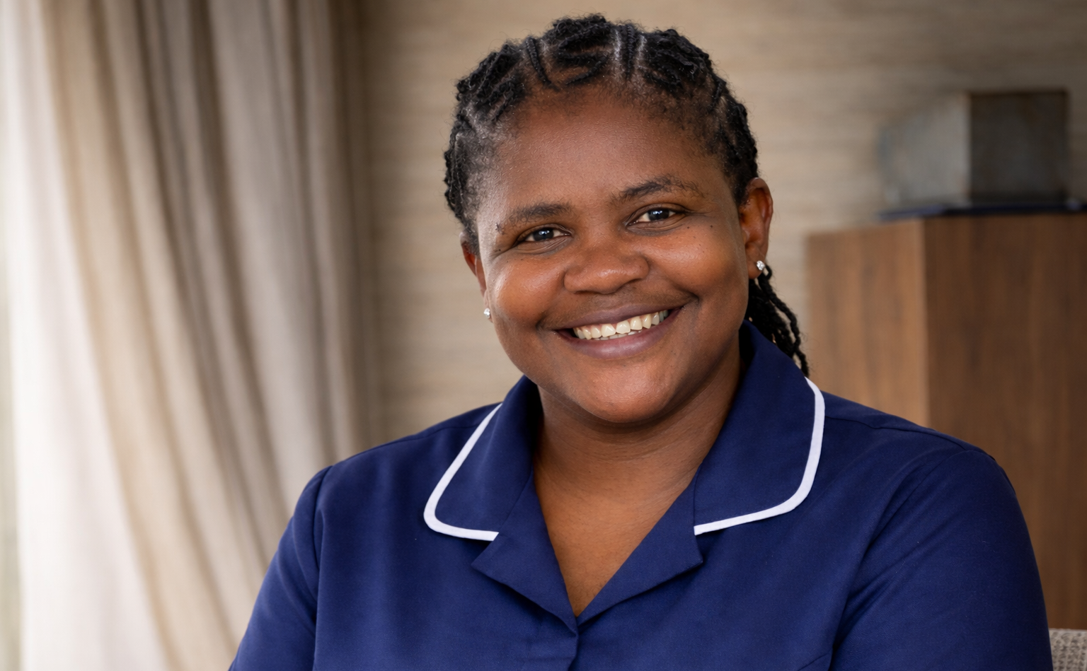 Woman in blue uniform smiles indoors.