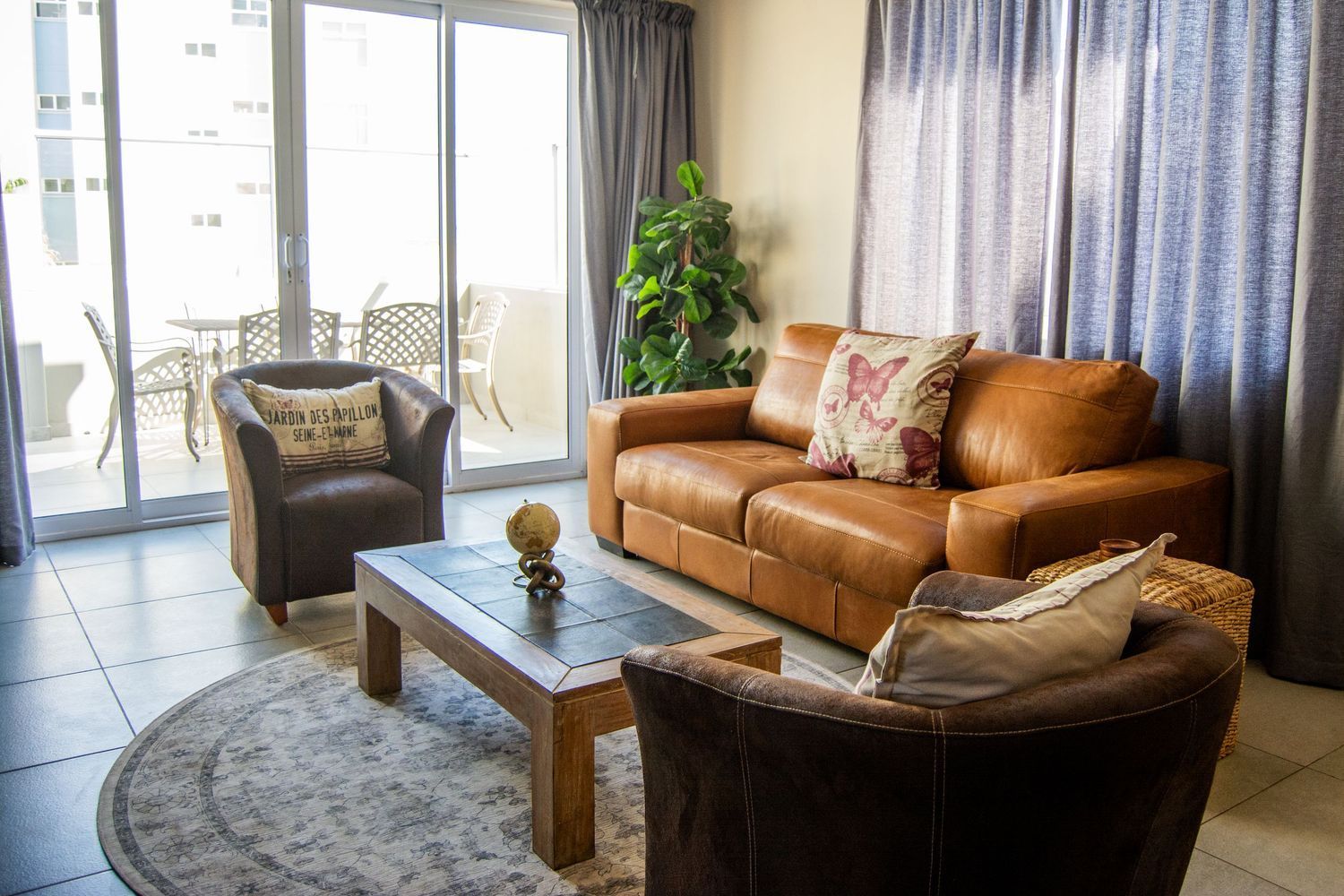 Living room with brown leather sofa, armchairs, coffee table, and sliding glass doors to a balcony.