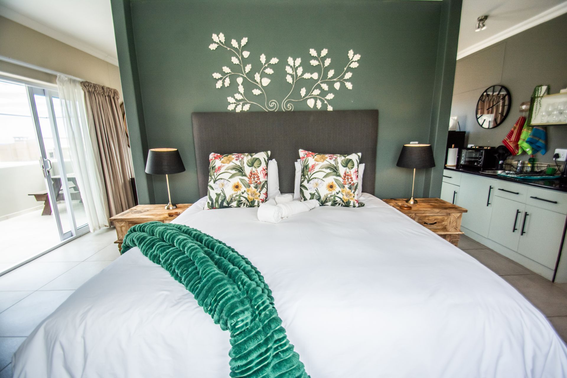Bedroom with bed, green accent wall, floral pillows, and balcony access.