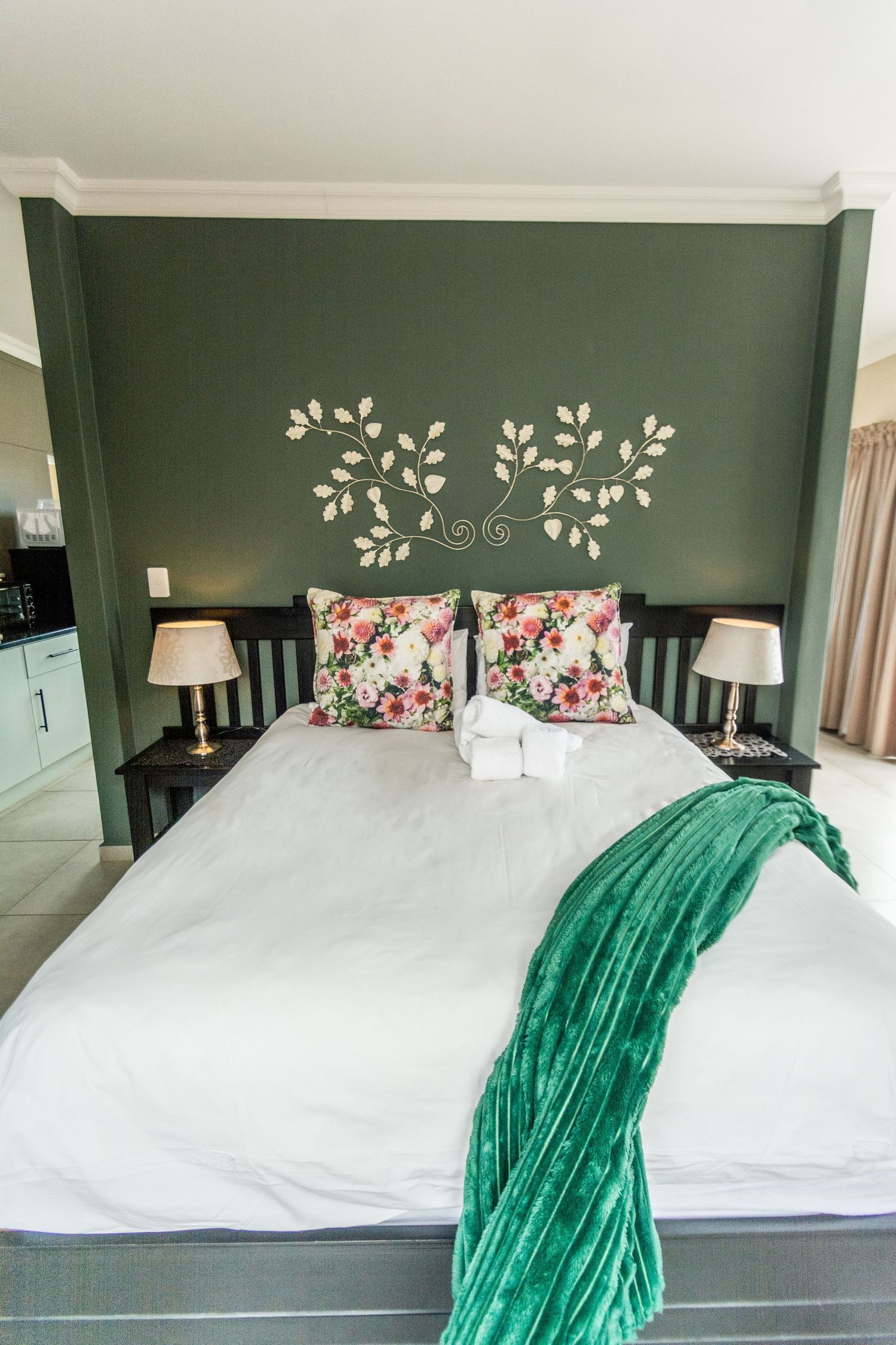 Bedroom with a dark green wall, white bedding, floral pillows, and a green throw.