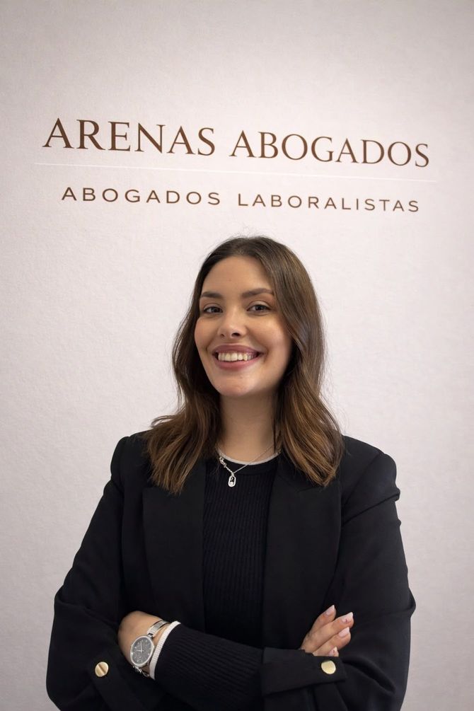 Mujer sonriendo con los brazos cruzados frente a un letrero de la oficina de Arenas Abogados.