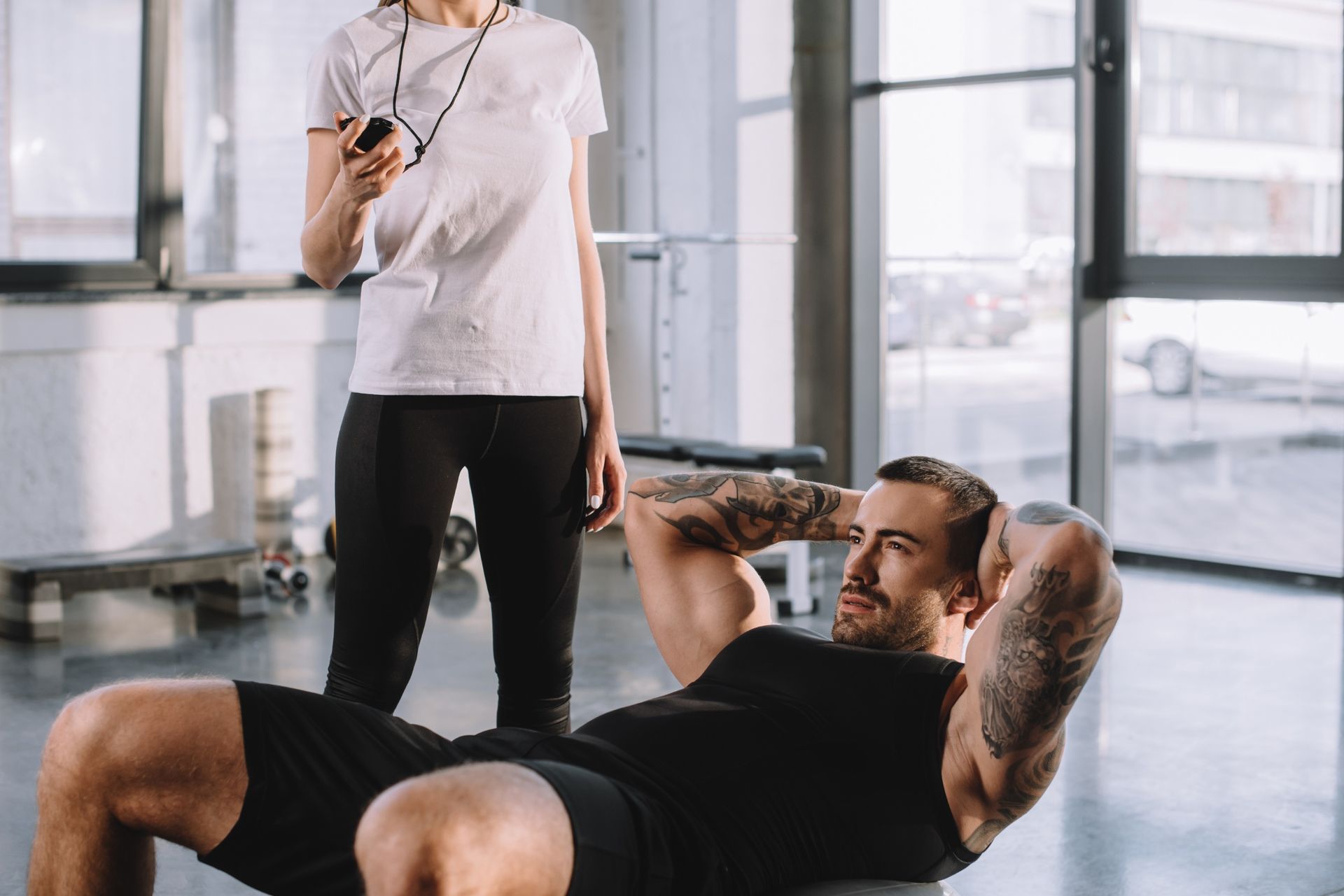 Un hombre está haciendo abdominales sobre una pelota en un gimnasio mientras una mujer observa.