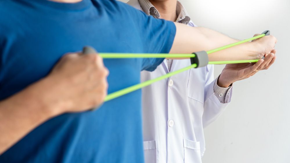 Un médico está ayudando a un paciente a estirar los brazos con una banda de resistencia.