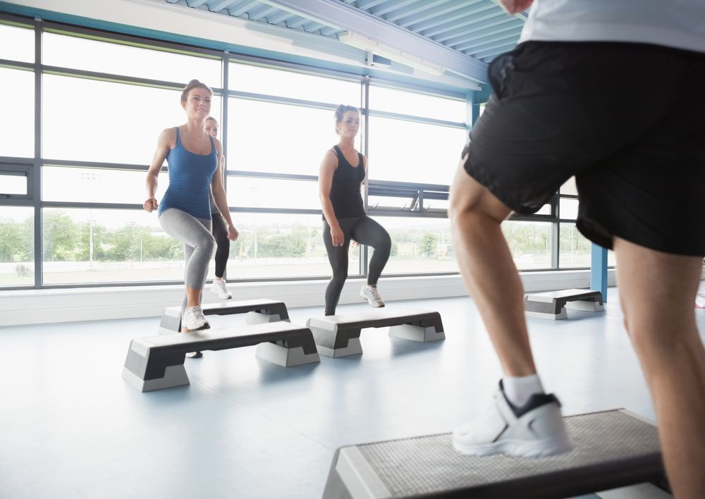 Un grupo de personas está haciendo step aeróbicos en un gimnasio.