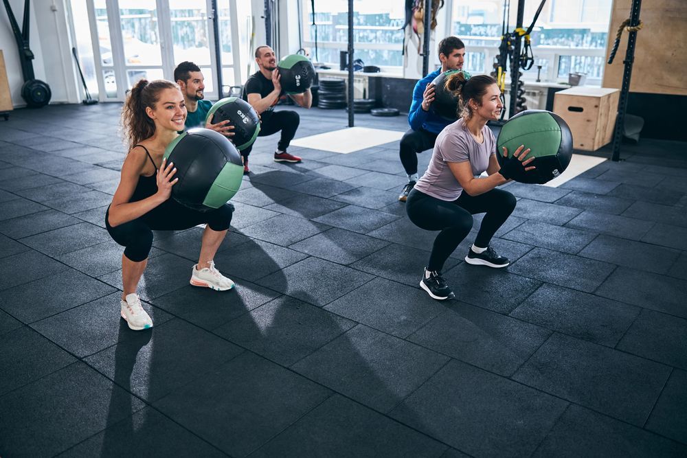 Un grupo de personas está en cuclillas con balones medicinales en un gimnasio.