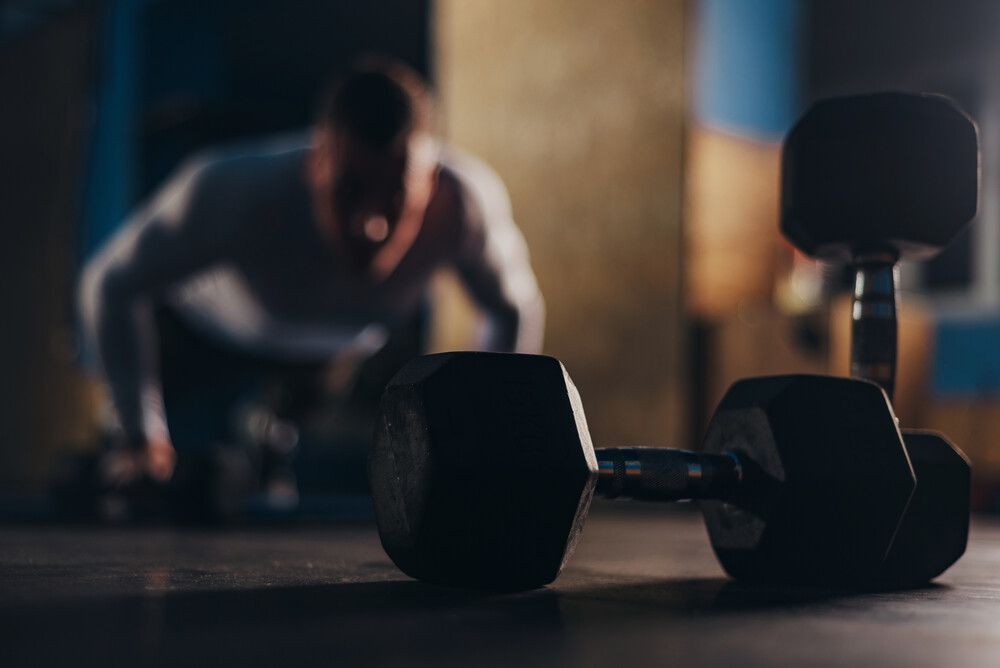 Un hombre está haciendo flexiones con mancuernas en el suelo en un gimnasio.