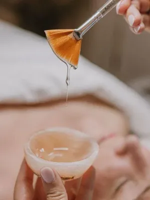 Una mujer está recibiendo un tratamiento facial con un cepillo y una taza de líquido.