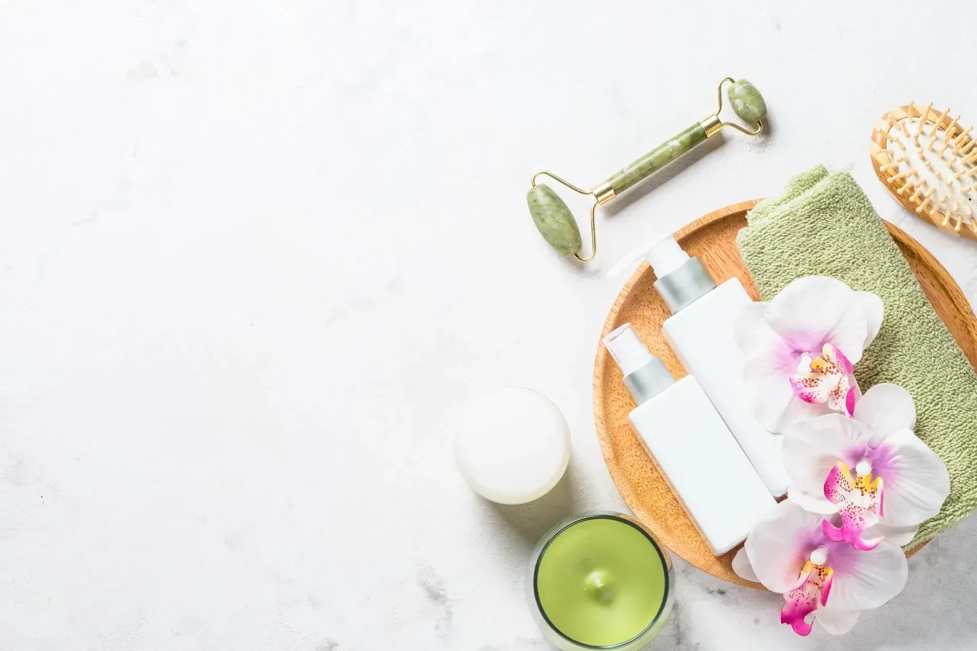 Una bandeja de madera llena de cosméticos, flores, velas y un rodillo de jade.