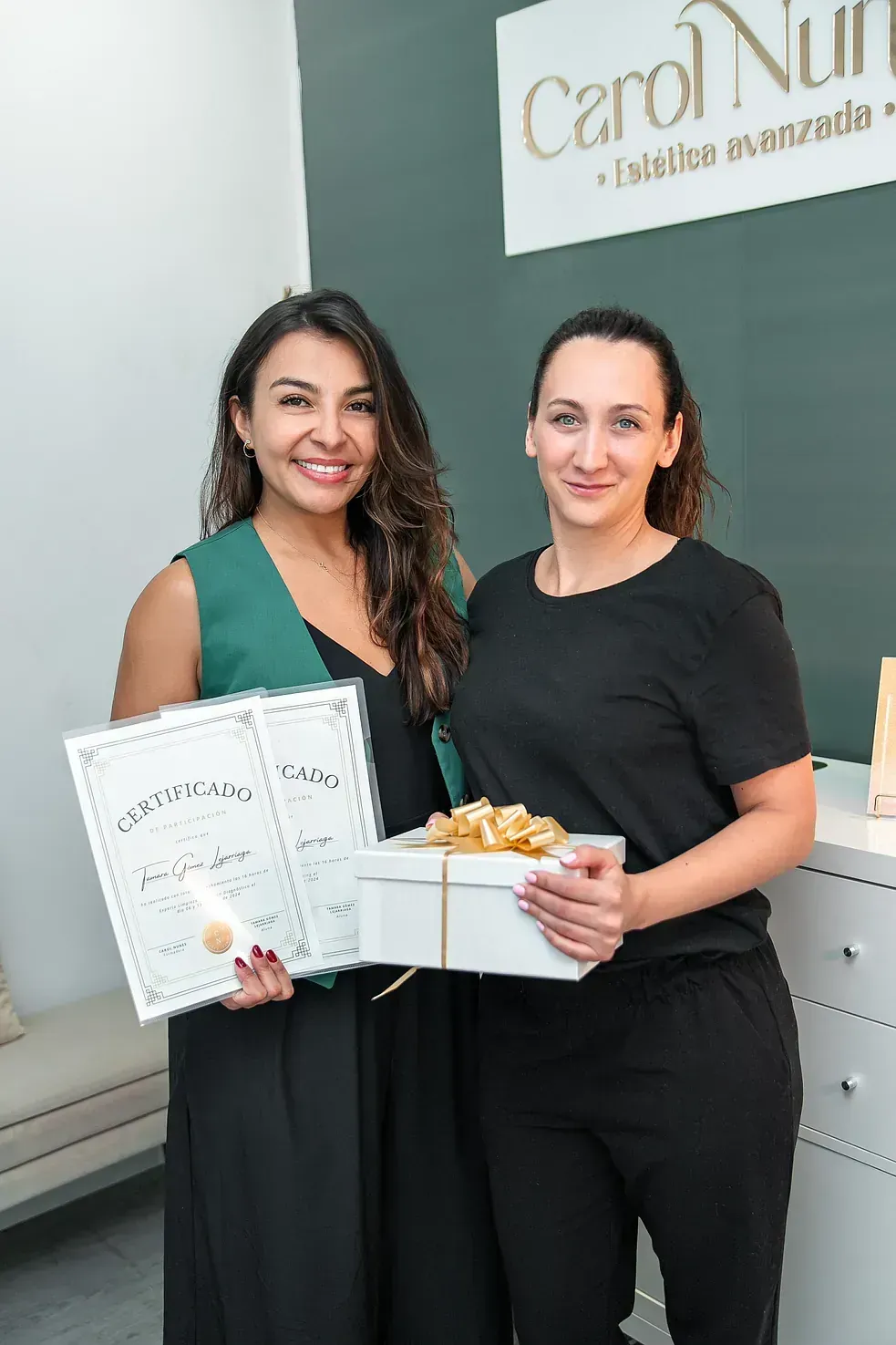 Dos mujeres están paradas una al lado de la otra sosteniendo un certificado y una caja de regalo.