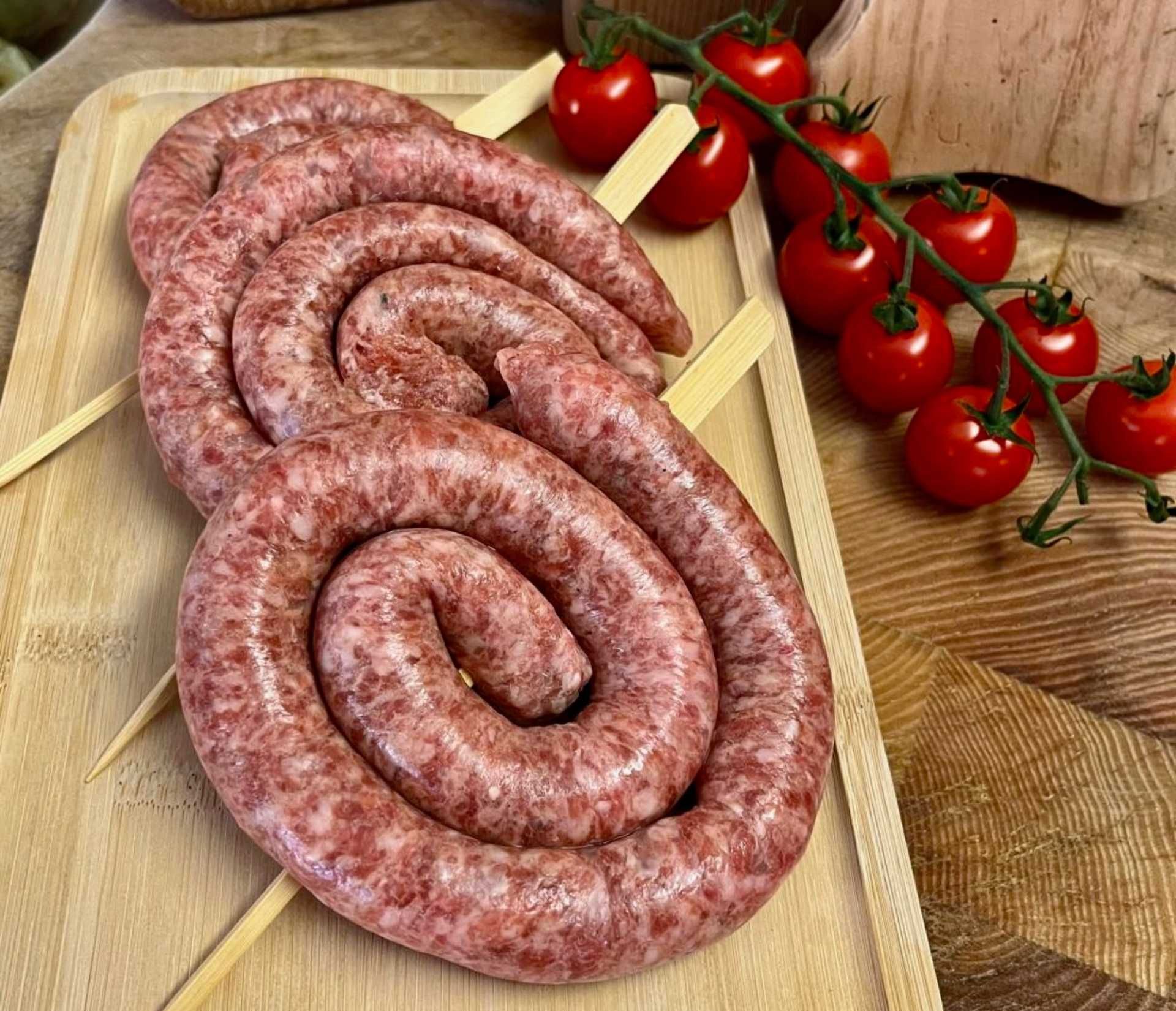 Une planche à découper en bois surmontée de saucisses et de tomates.