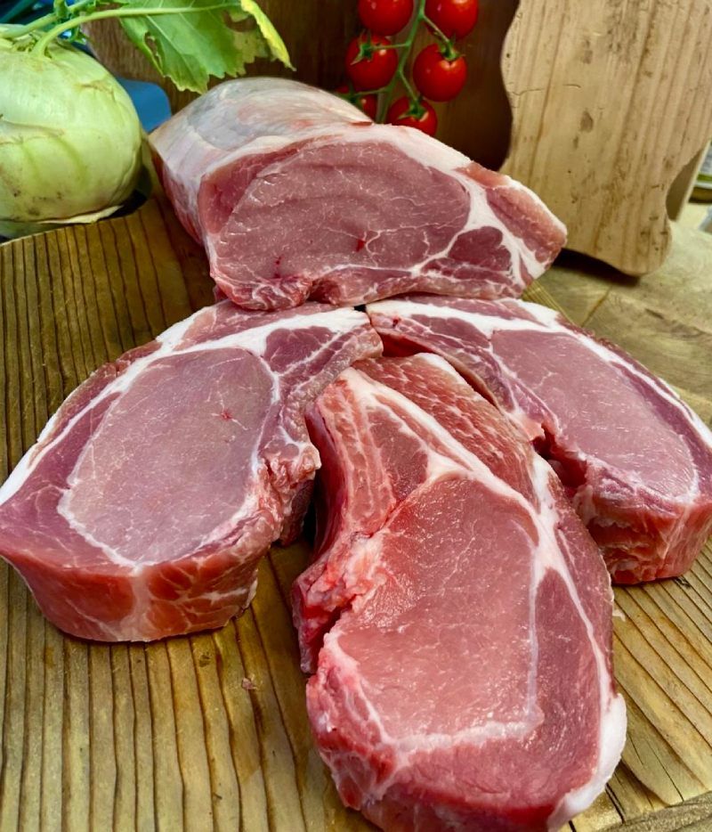 Un tas de côtelettes de porc crues sur une planche à découper en bois