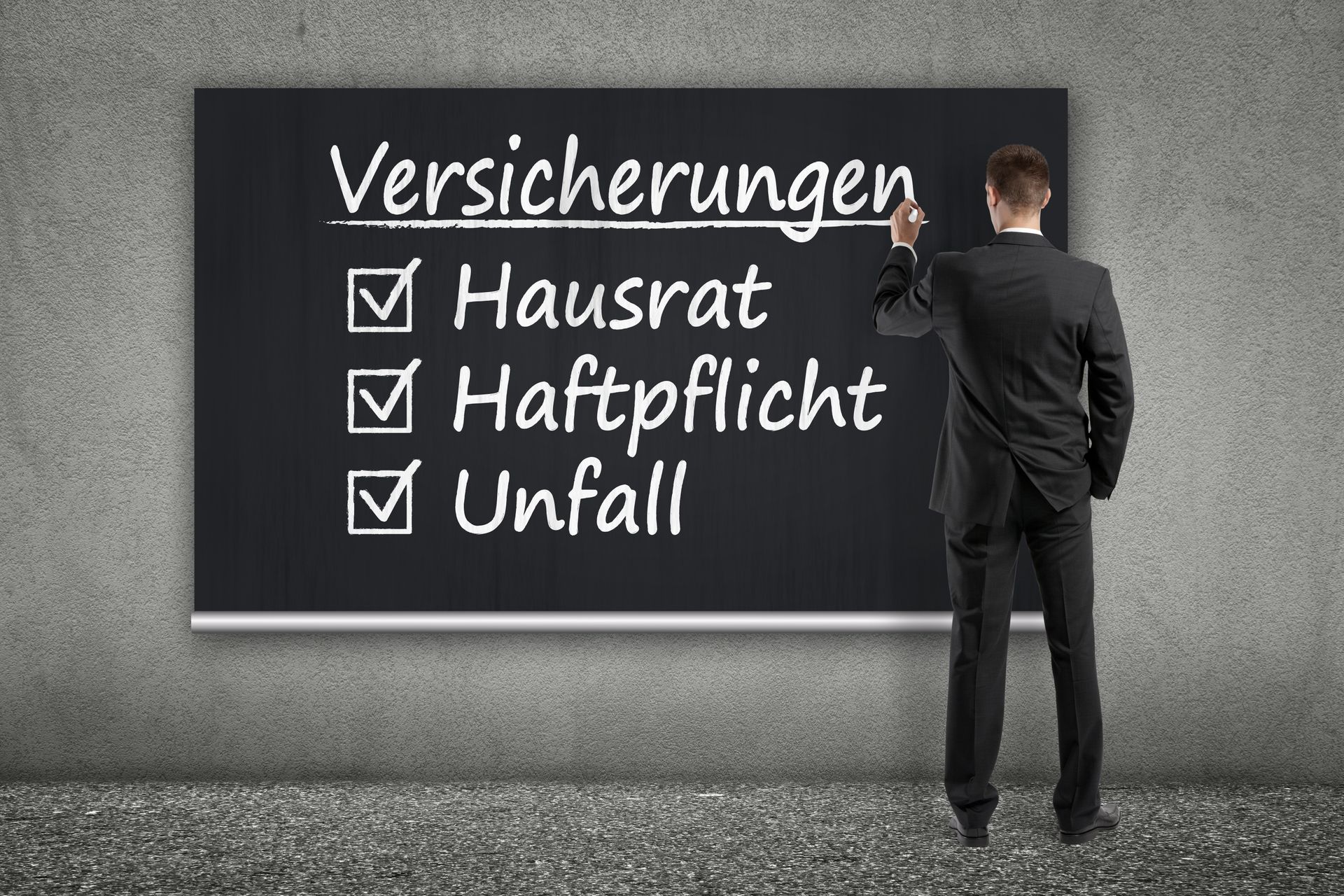 Kleines Hausmodell neben Klemmbrett und Telefon auf einem Schreibtisch, im Hintergrund sind Personen verschwommen zu erkennen.