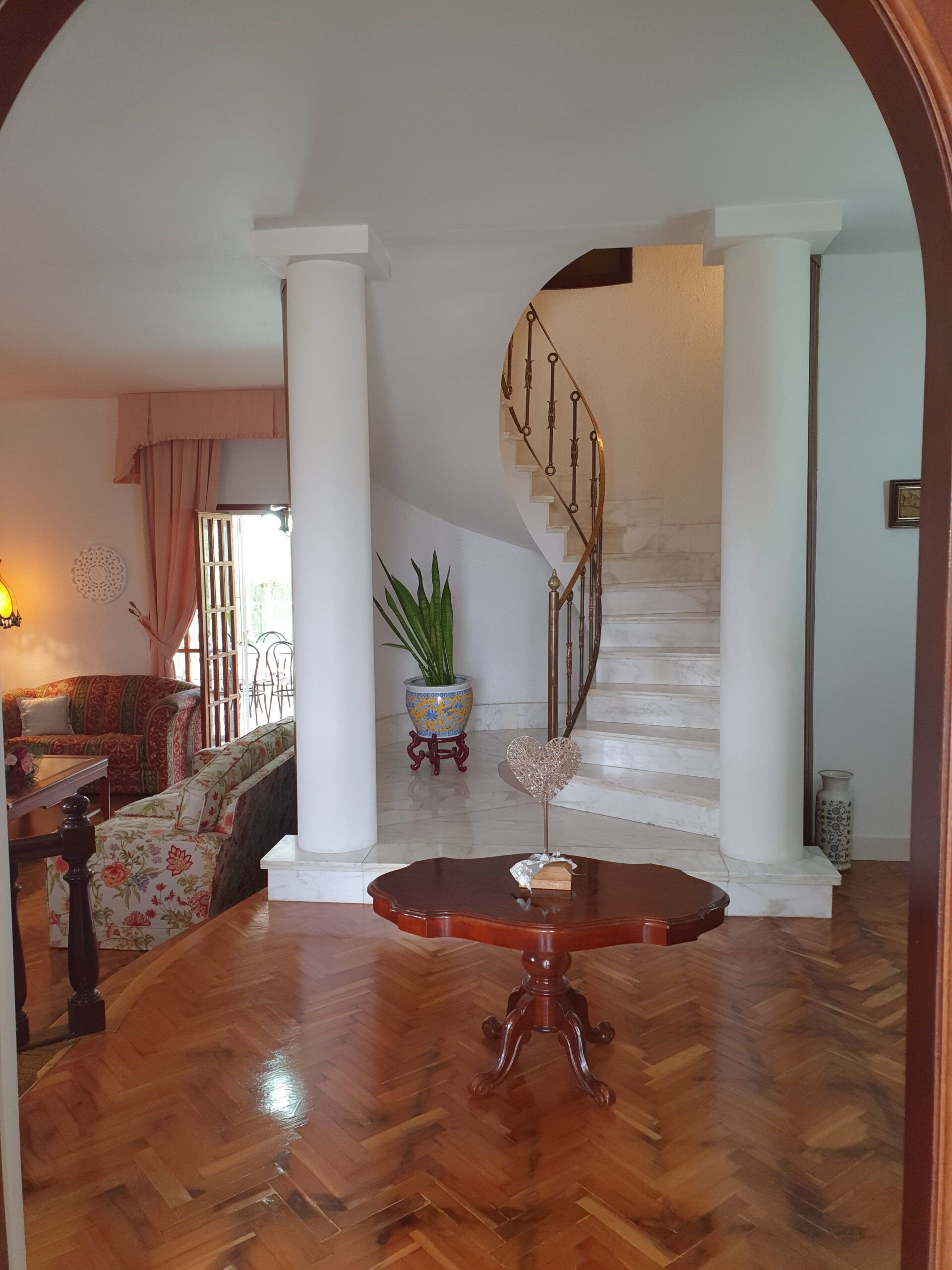 Elegante salón con columnas blancas, escalera de caracol y suelo de madera pulida.
