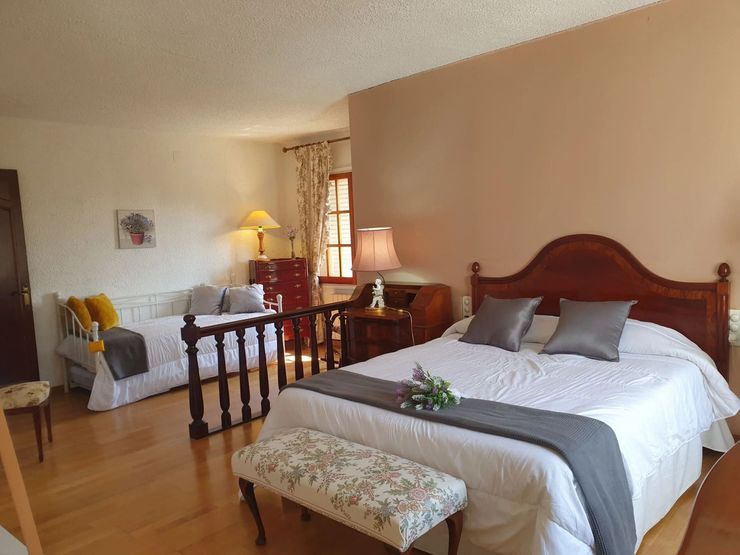 Dormitorio con una cama grande, cabecero de madera y zona de estar en tonos beige cálidos.