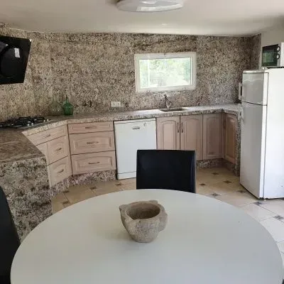 Cocina con paredes de piedra moteada, armarios blancos, una mesa redonda y un frigorífico blanco.