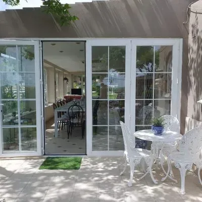 Patio blanco con puertas de cristal, mesa y sillas blancas, y vistas a un luminoso comedor interior.