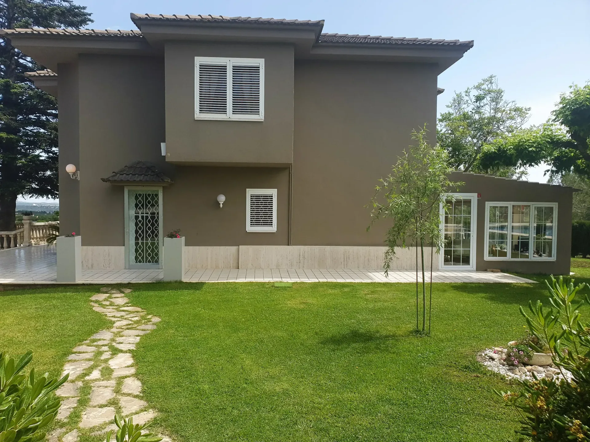Casa gris de dos plantas con césped verde, camino de piedra y pequeñas ventanas delanteras.
