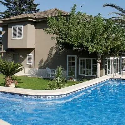Casa moderna junto a una piscina azul con césped verde y árboles.