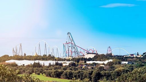 Horizonte de un parque de atracciones con montañas rusas sobre los árboles bajo un cielo azul despejado.