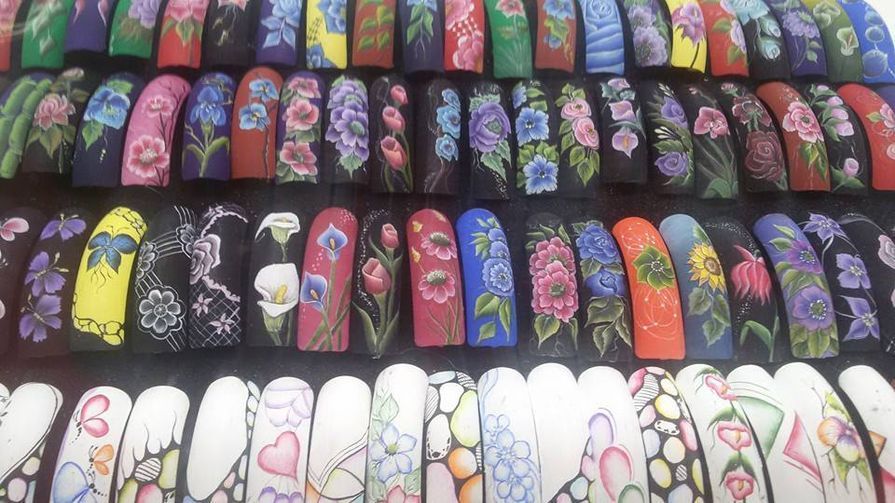 Fileiras de unhas postiças coloridas, pintadas com motivos florais.