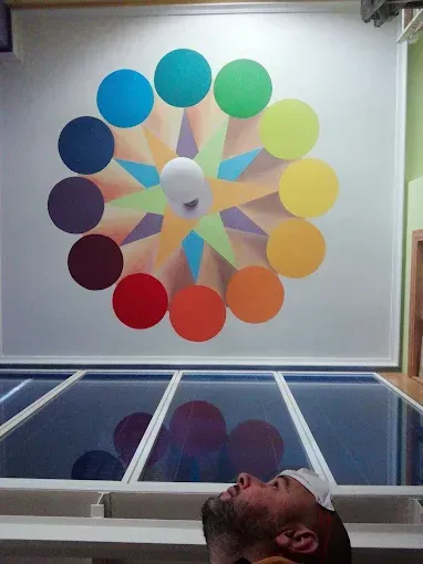 Hombre mirando hacia una rueda de color en una pared, círculos coloridos dispuestos alrededor de una luz central.