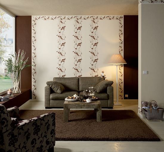 Sala de estar con sofá marrón, alfombra y papel pintado estampado. La luz del sol entra a raudales.