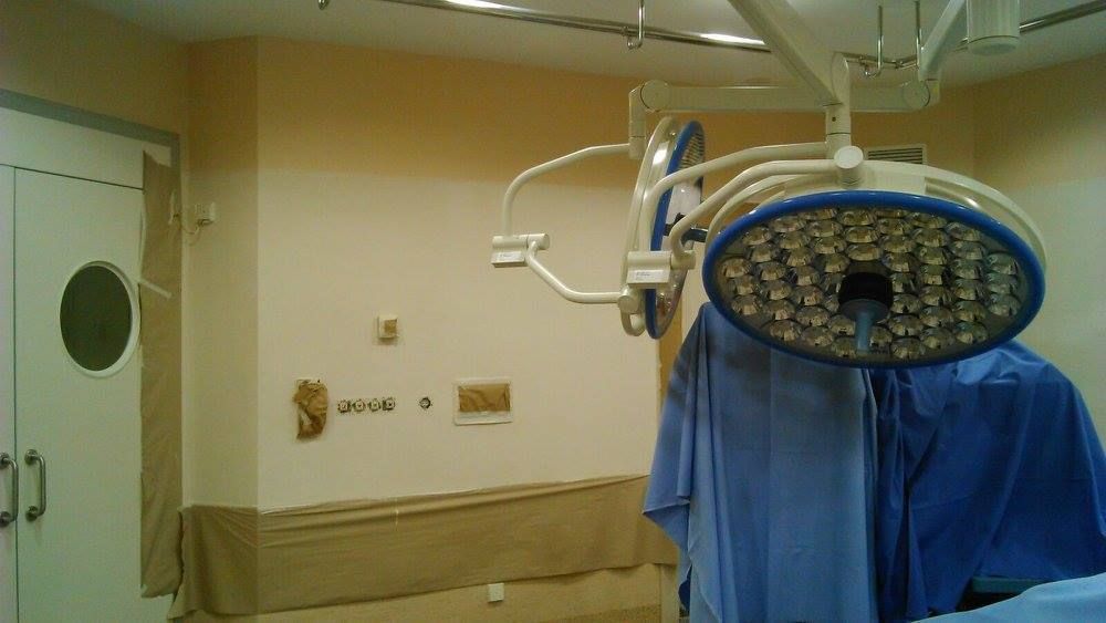 Una sala de operaciones con una lámpara quirúrgica, cortinas azules y una puerta cerrada.