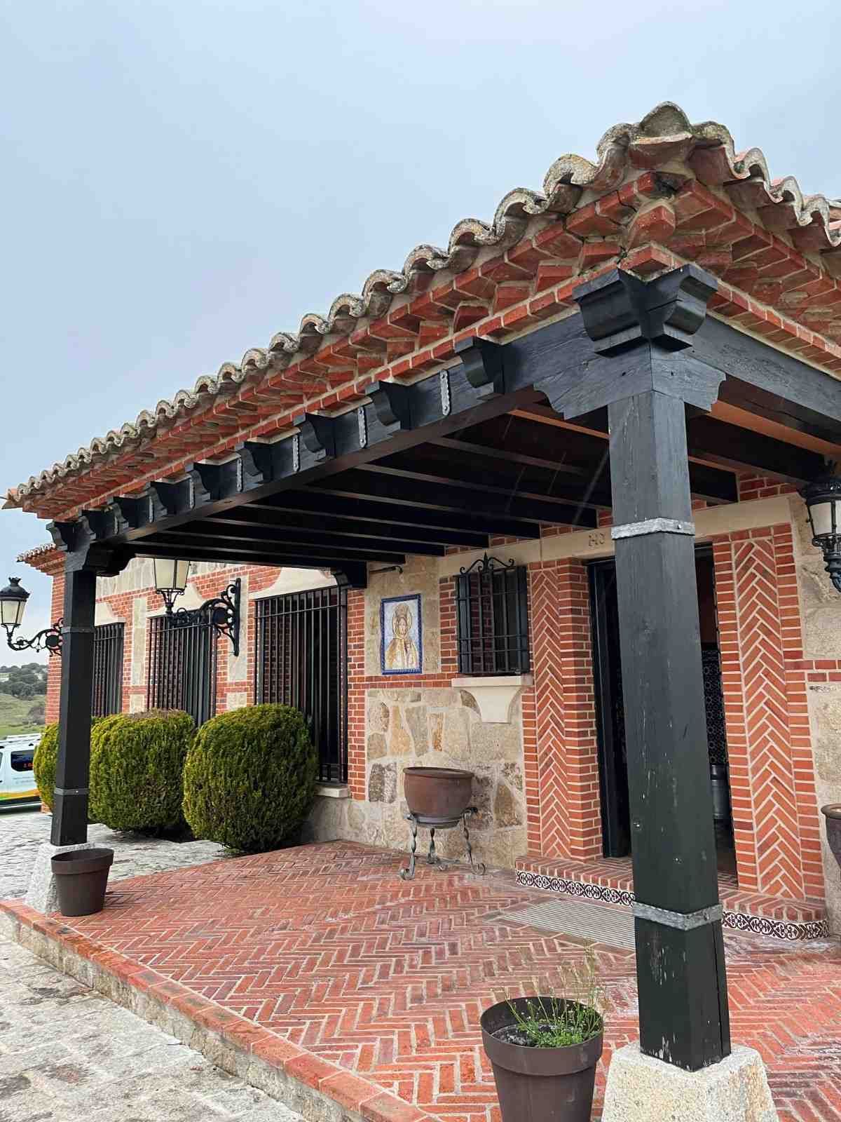 Edificio de ladrillo con soportes de madera negra y techo de tejas rojas, plantas en macetas en el frente.