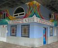 Un edificio azul con un mural colorido, bajo un paso elevado. Letrero
