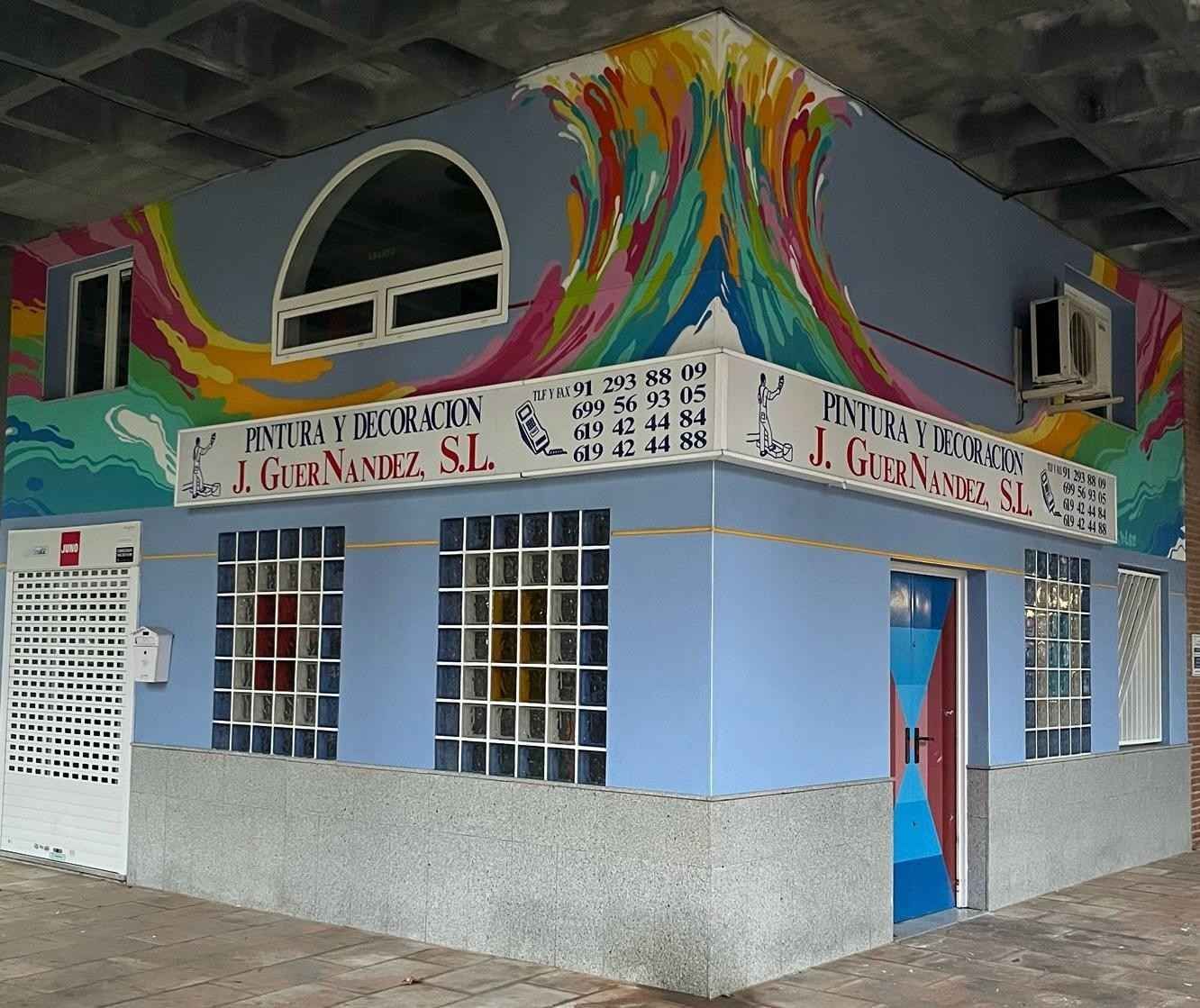 Un edificio azul con un mural colorido, bajo un paso elevado. Letrero 