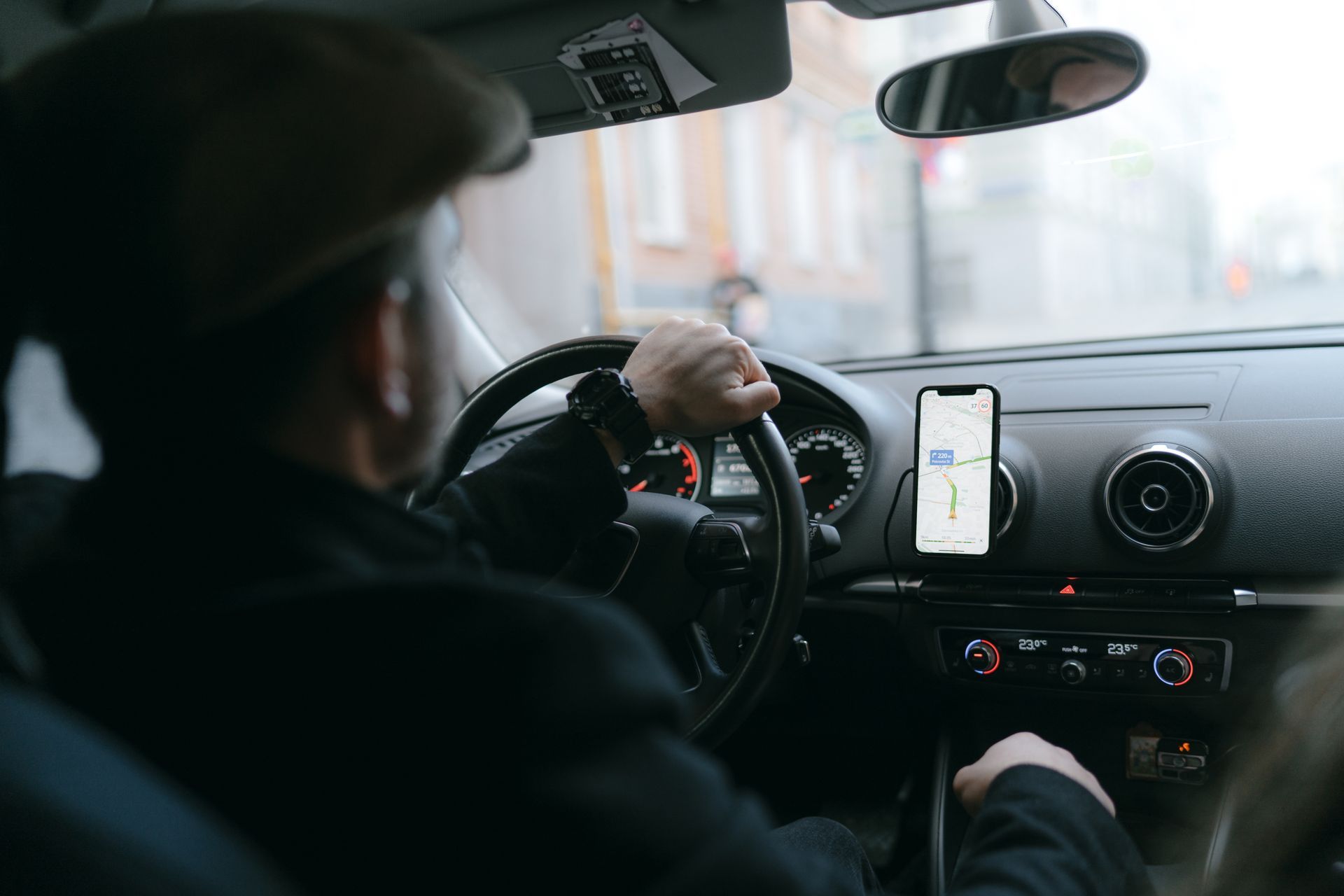 Une personne au volant d'une voiture, tenant le volant, son téléphone avec l'application de navigation visible.