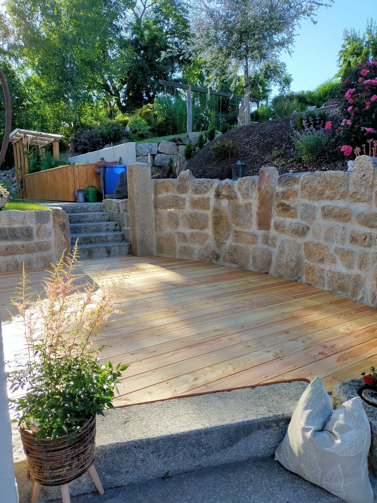 Terrasse mit Holzboden und Natursteinumrandung und Treppen zum höher gelegenen Garten