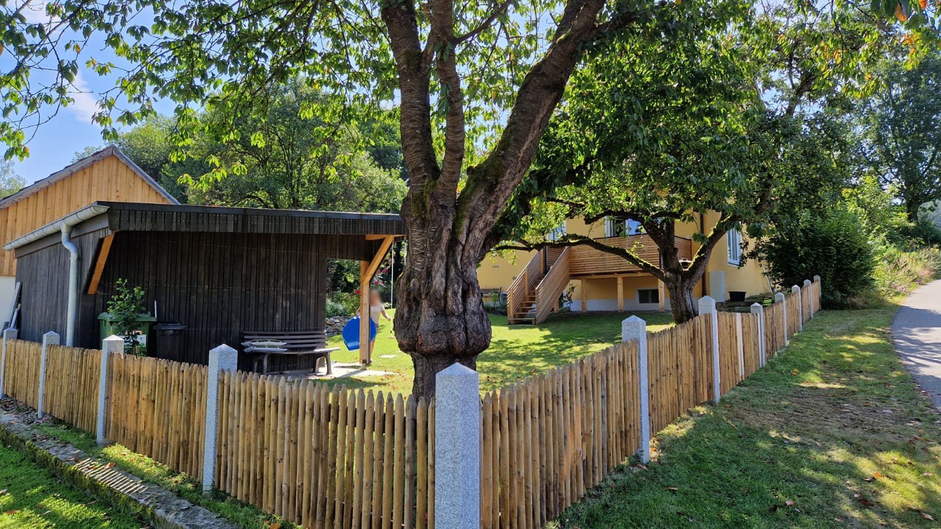 Halbhoher Gartenzaun aus Palisadenhölzern unterbrochen durch Steinsäulen 