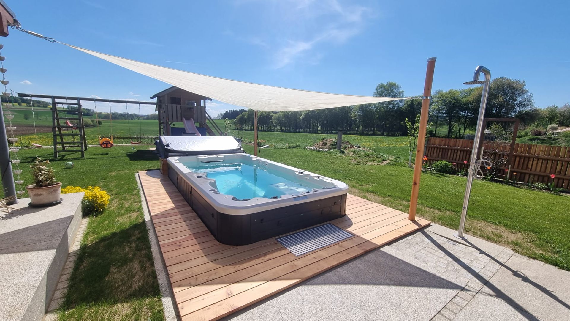 Großer Pool in einem Garten auf einer Holzterrasse mit einem aufgespannten Sonnensegel