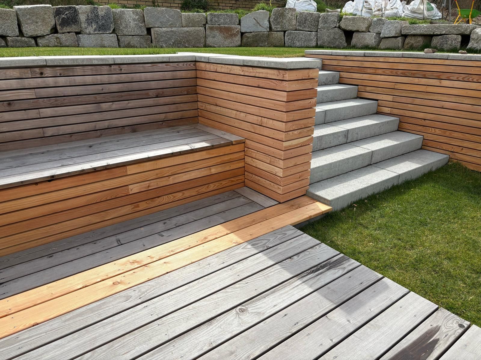 Terrasse aus Holzplanken mit eingebauter langer Sitzbank und Steintreppen zum höhergelegten Garten