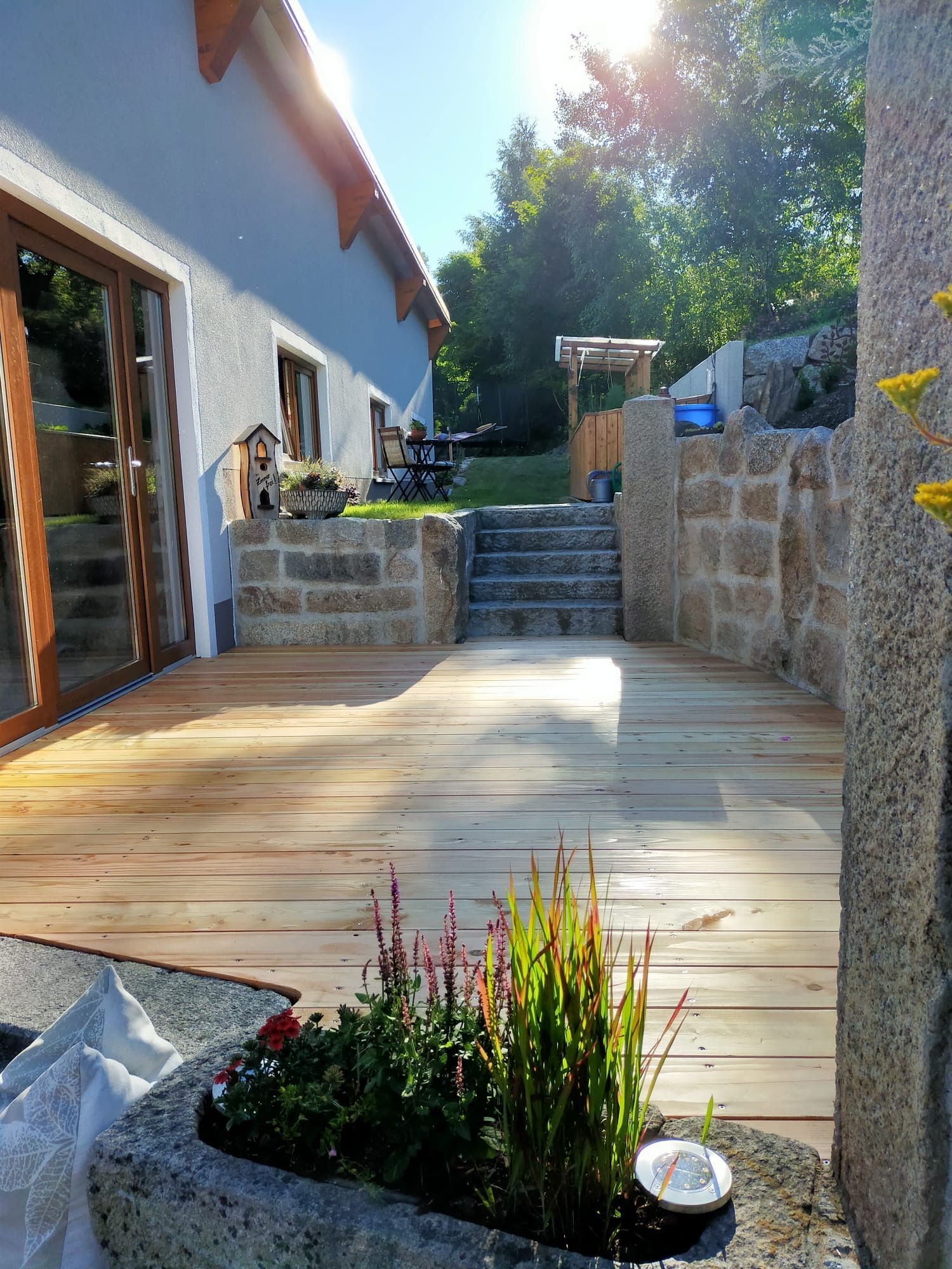 Terrasse mit Holzboden und Natursteinumrandung und Treppen zum höher gelegenen Garten