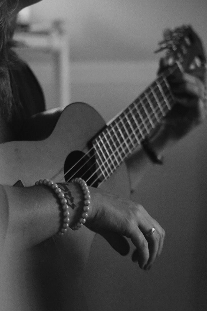Persona tocando un ukelele, luciendo pulseras de perlas.