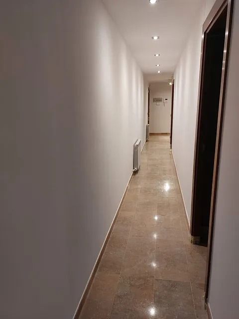 Un largo pasillo con suelo de mármol y paredes blancas.