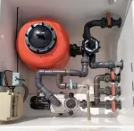 Una caja blanca con muchas tuberías y un tanque naranja.