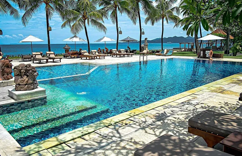 Una gran piscina rodeada de palmeras junto al océano.