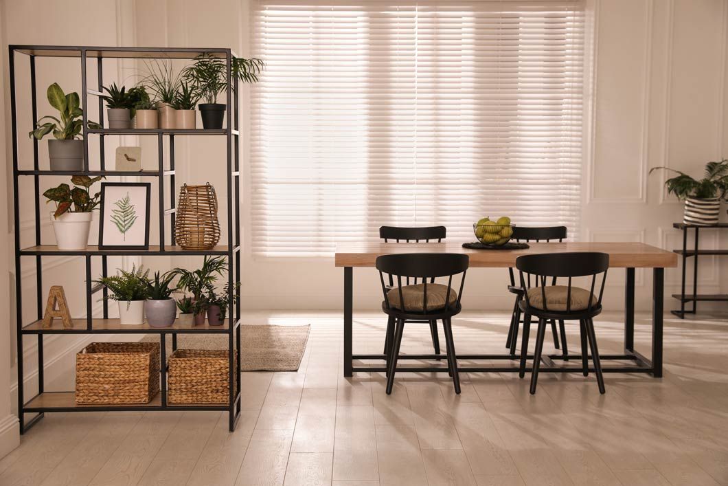 Un comedor con una mesa y sillas y una estantería llena de plantas en macetas.